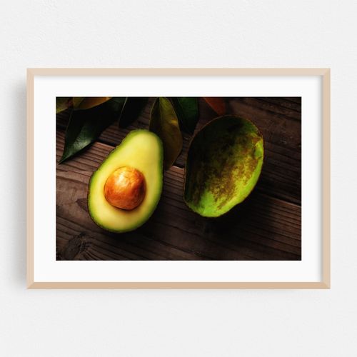 An Avocado cut in half on a wood surface with leaves. One half s